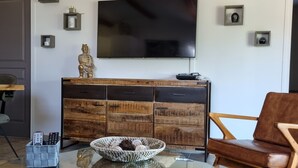 Ein Wohnzimmer mit Glastisch, Holzschrank, Ledersofa und einem an der Wand montierten Flachbildfernseher.