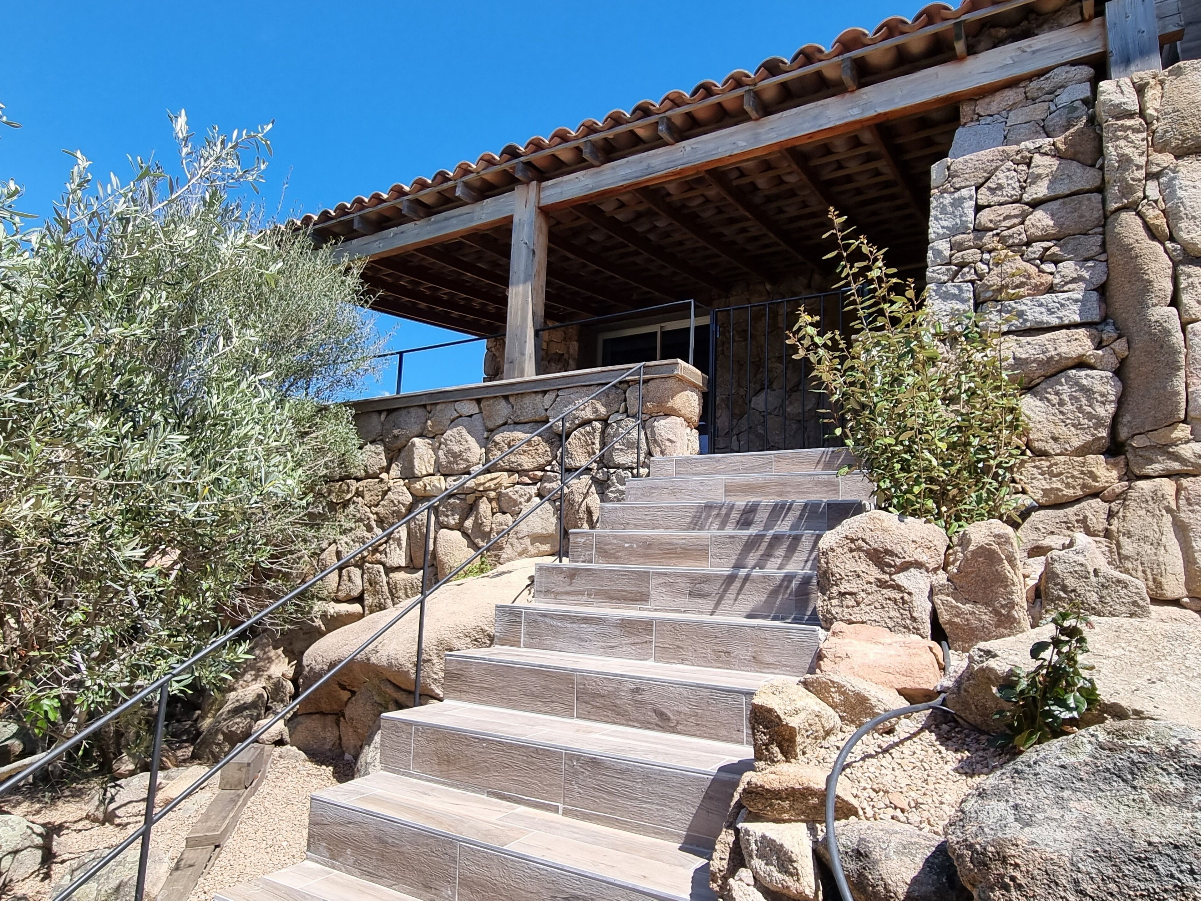 A stone staircase leading to a wooden-roofed building with a metal railing.