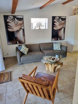 Ein modernes Wohnzimmer mit einem grauen Sofa, zwei großen Wandbildern, einem Glastisch mit einem gewebten Korb und einem Holzstuhl.