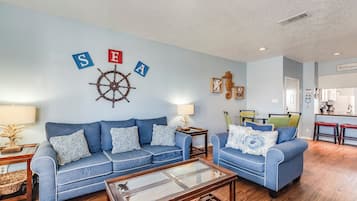 Una sala de estar con un sofá azul, una mesita de centro y decoración náutica, incluyendo un timón y letras del alfabeto.