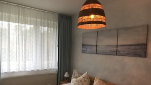 A bedroom with a bed, pillows, a hanging lamp, a window with curtains, and a painting on the wall. - Last minute offer vacation apartment directly on the lake, near Berlin (Lünow)