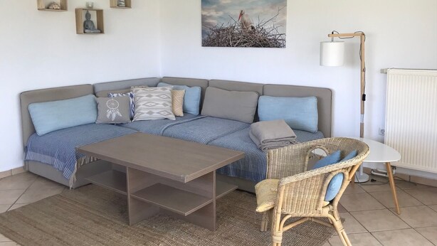 A corner living room with a sofa, a coffee table, a wicker chair, a floor lamp, and a painting on the wall. - Last minute offer vacation apartment directly on the lake, near Berlin (Lünow)