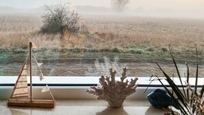 A view from a window overlooking a foggy field with a wooden balance scale, a coral sculpture, and a fish figurine on a windowsill. - Last minute offer vacation apartment directly on the lake, near Berlin (Lünow)