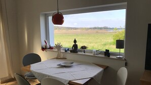 A dining area with a table set for four, a window with a view of a green field, and a Buddha statue on the windowsill. - Last minute offer vacation apartment directly on the lake, near Berlin (Lünow)