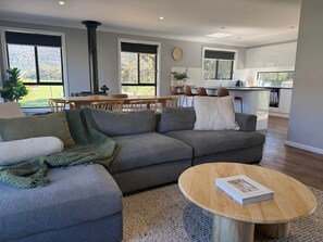 A modern living room with a grey sectional sofa, a round wooden coffee table, and a dining area with a wooden table and chairs.