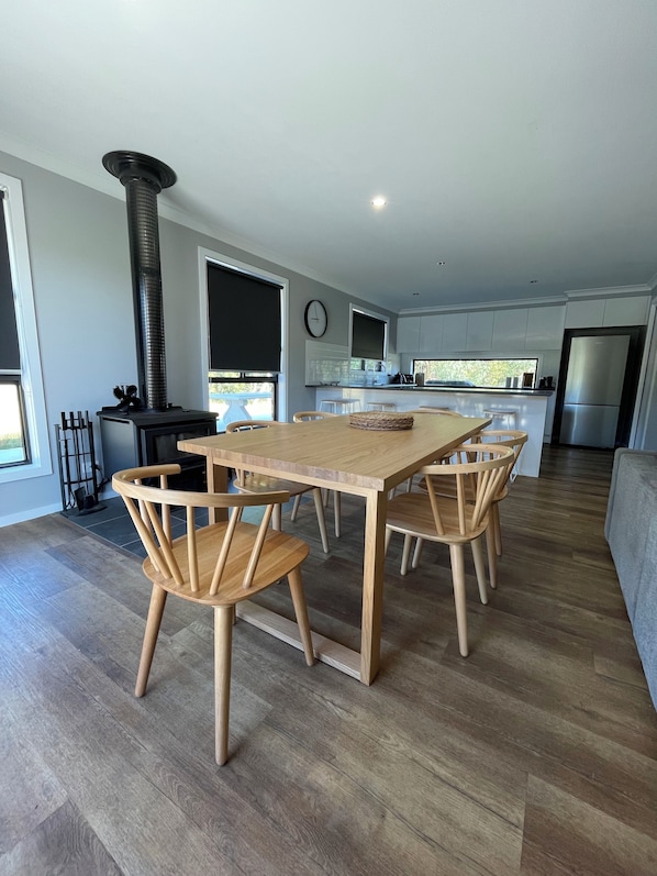 A modern kitchen with a central island, wooden chairs, and a large window. - Piccolo Retreat (Halls Gap)