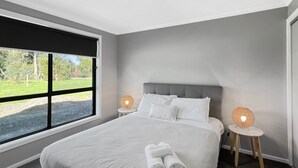 Un dormitorio moderno con una cama grande, vista a un paisaje verde por una ventana y dos lámparas de noche.