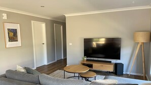 Una sala de estar moderna con un sofá seccional gris, una mesa de centro de madera, un televisor de pantalla plana sobre un soporte de madera y una lámpara de pie.