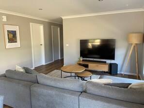 A modern living room with a grey sectional sofa, a wooden coffee table, a flat-screen TV on a wooden stand, and a floor lamp.