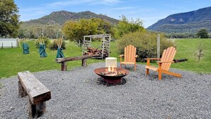 Un espacio al aire libre con una chimenea, sillas de madera y un banco.