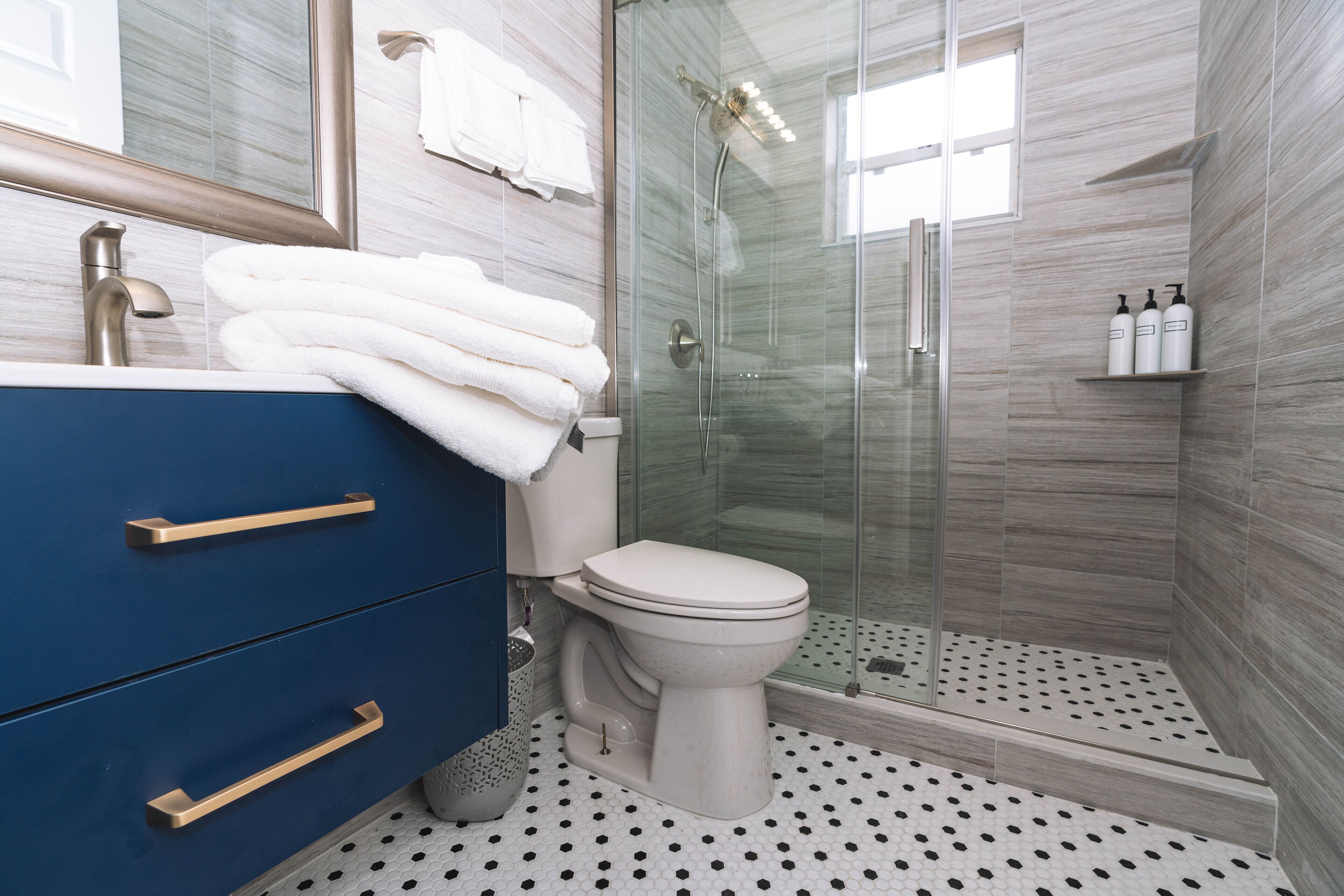 Een badkamer met een douchecabine van glas, een wit toilet en een blauwe wastafel met gouden knoppen.