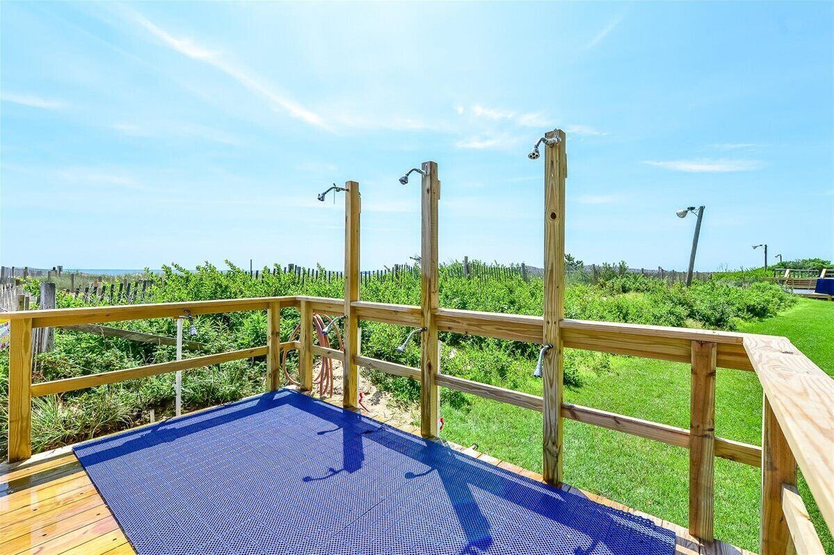 A wooden deck with a blue mat, surrounded by a wooden fence, overlooking a grassy area with a clear sky.