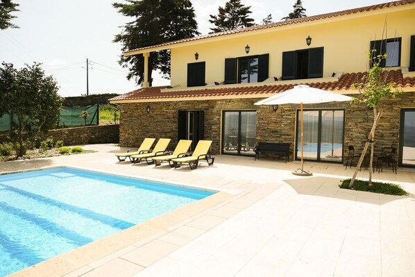 Edificio de dos pisos con piscina, mobiliario exterior y fachada de piedra.