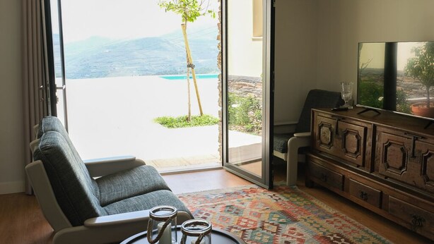 A living room with a sofa, a coffee table with candles, a TV, and a view of a mountain and sea through a glass door.