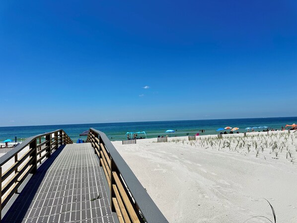 Walk along the beachside path to a serene beach area with umbrellas and chairs.
