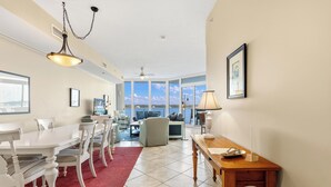 A spacious living area with a dining table, chairs, a red rug, a wooden side table, and a view through large windows. - Lagoon Front 3 bed 3 bath unit!  Call today New to rental Market. (Gulf Shores)