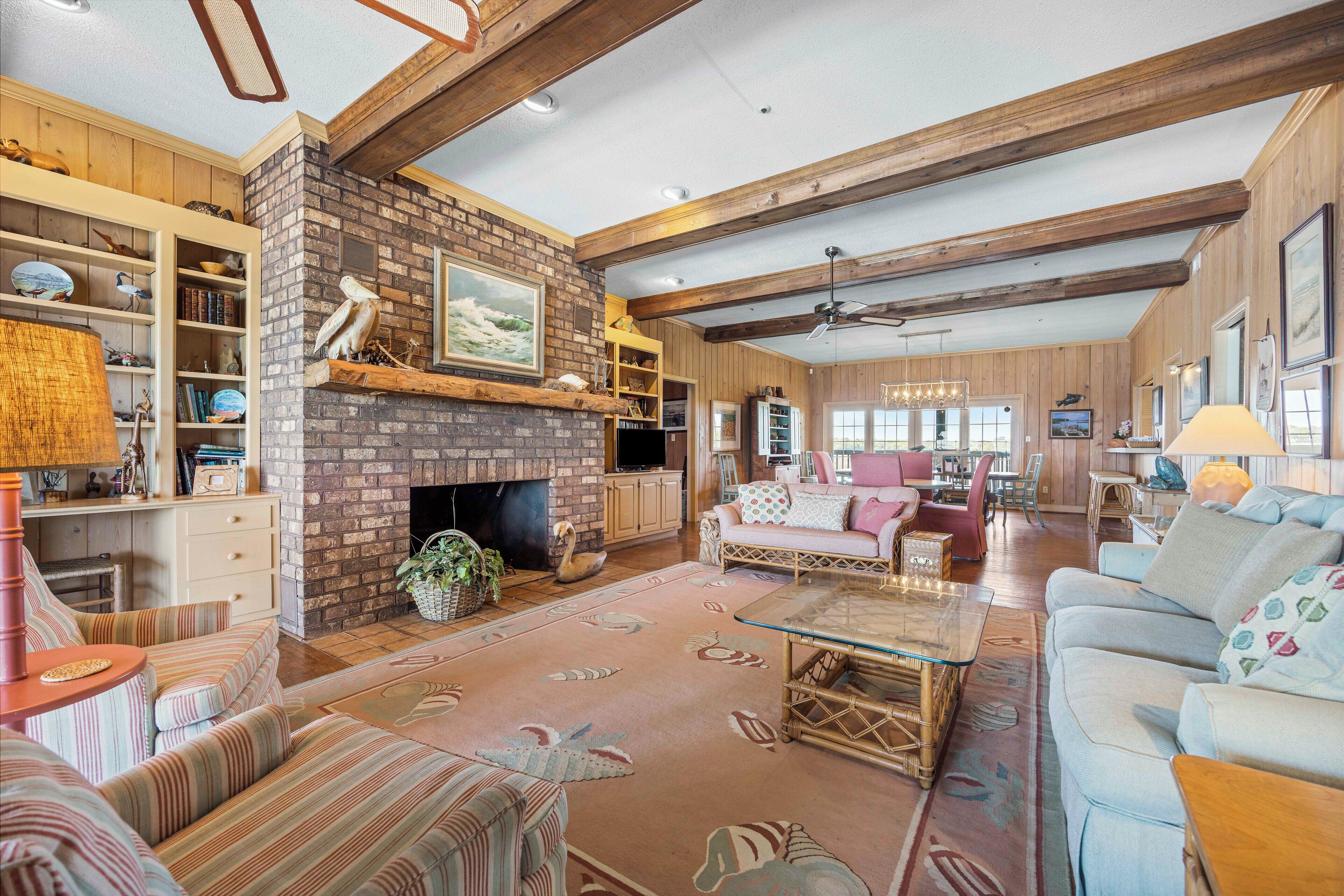 A spacious living room with a brick fireplace, wooden beams, and a cozy seating area with sofas and a coffee table.