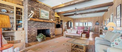 A spacious living room with a brick fireplace, wooden beams, and a cozy seating area with sofas and a coffee table.