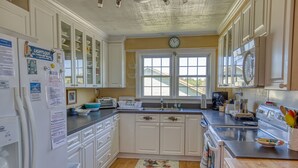 Une cuisine avec des meubles blancs, un évier, une cuisinière et une horloge au mur.