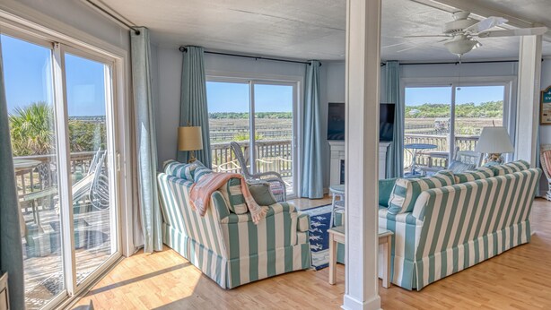 Un salon spacieux doté de grandes fenêtres, d’un ventilateur de plafond et offrant une vue sur la plage.