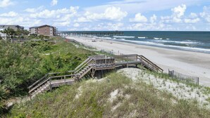Une plage avec une promenade en bois menant à la rive, une jetée s’avançant dans l’océan et des bâtiments en arrière-plan.