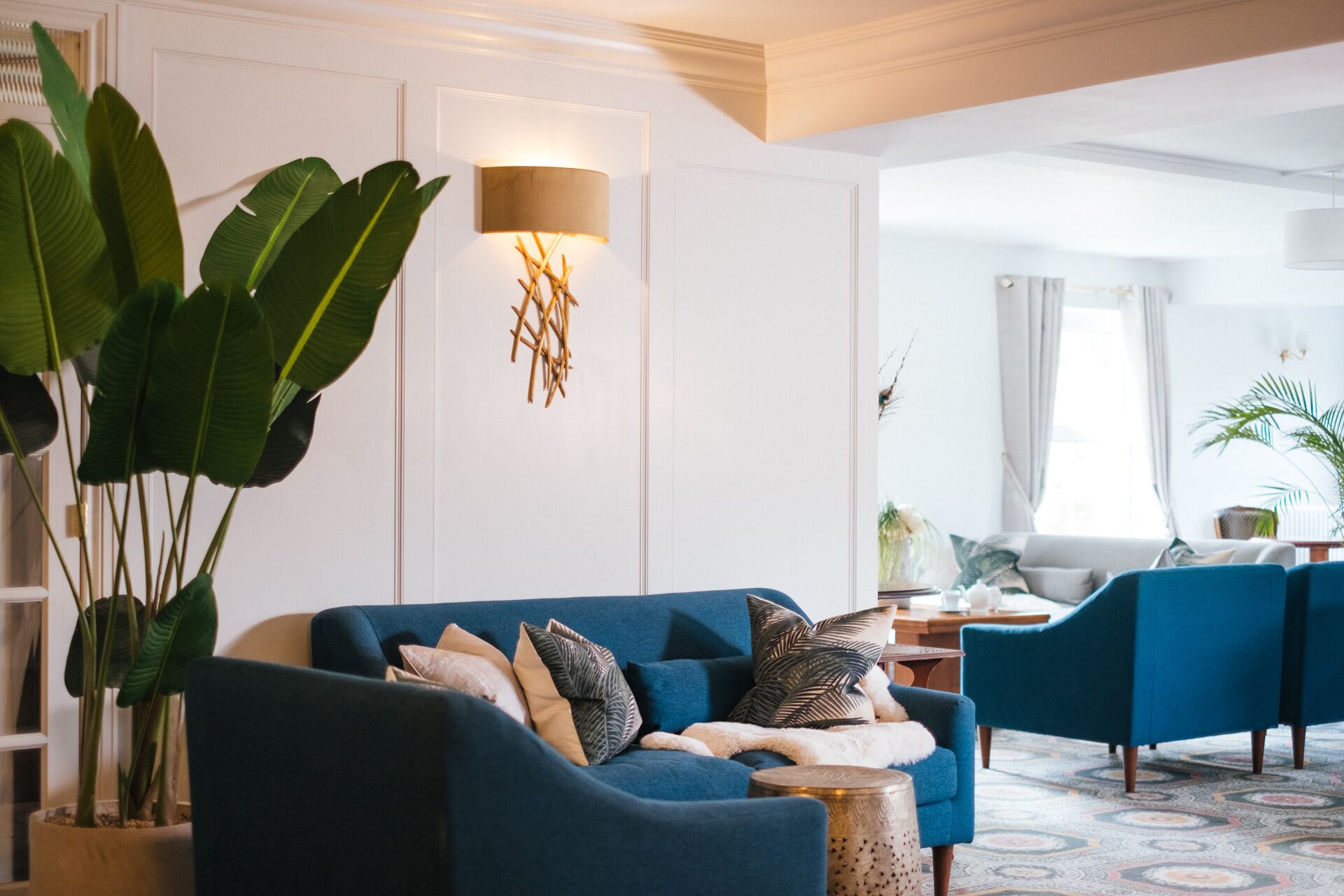 Un salon moderne avec un canapé bleu, des coussins décoratifs, une table d’appoint et une grande plante.