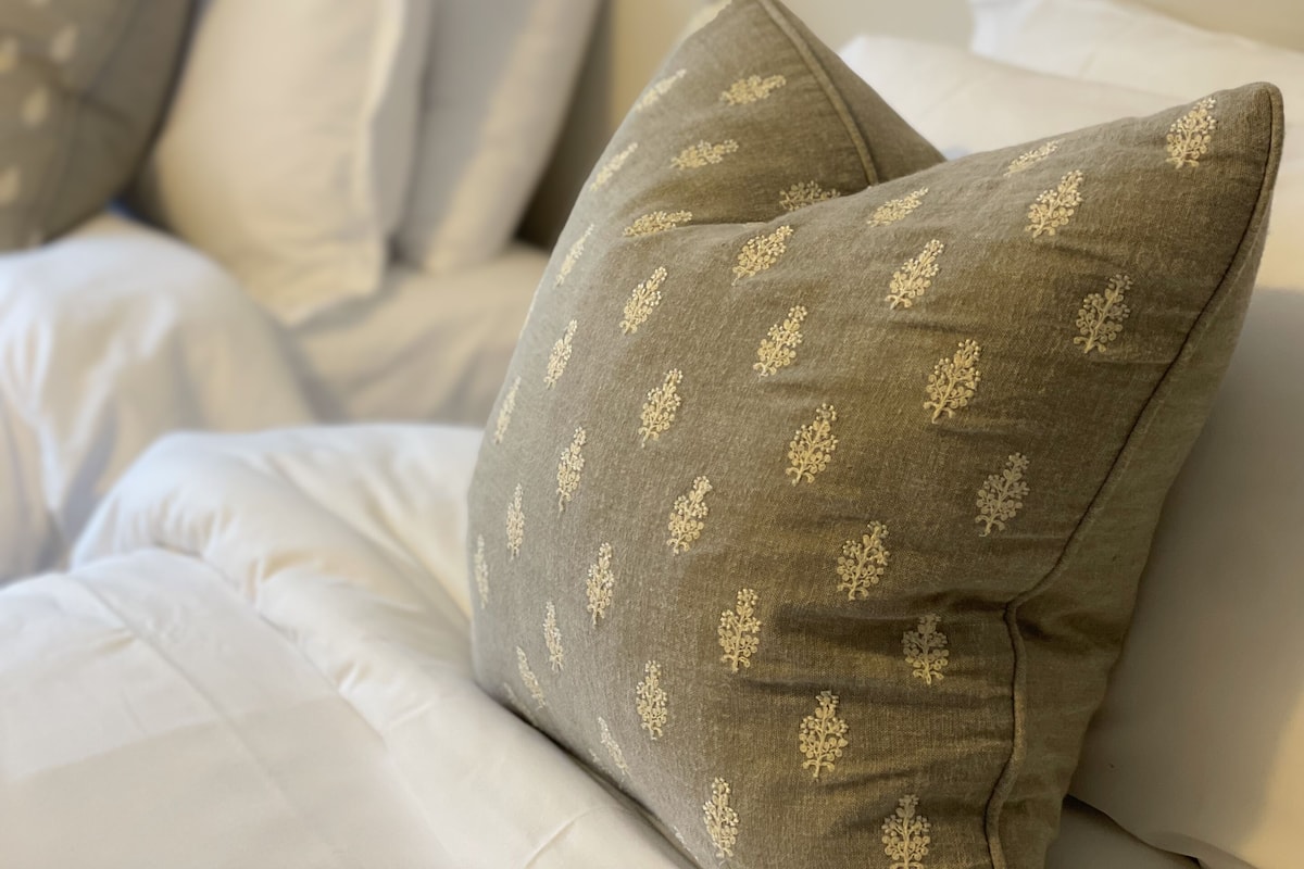 A bed with white bedding and multiple pillows, some with a floral pattern.