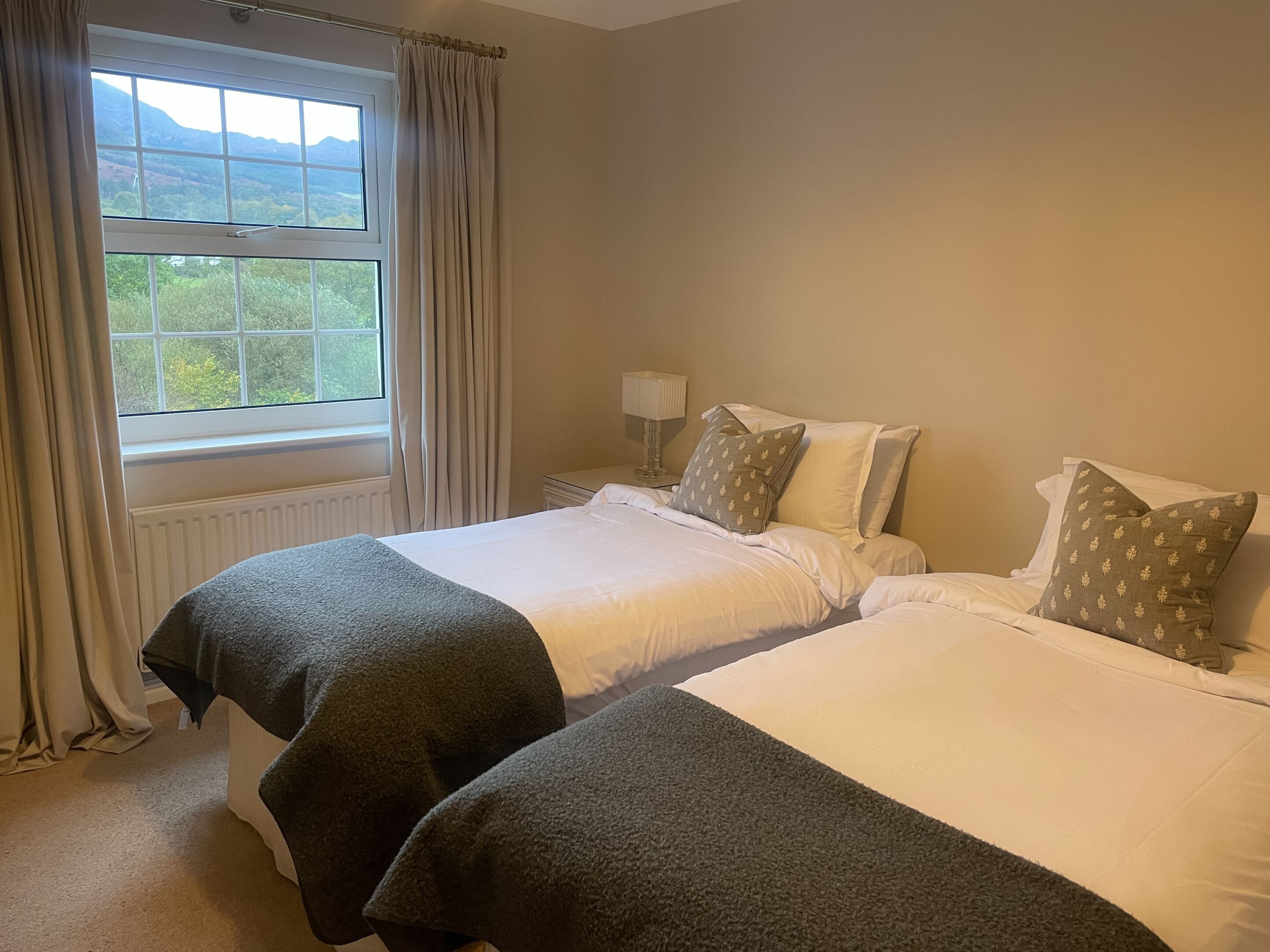 Une chambre d’hôtel avec deux lits, une fenêtre avec des rideaux, une table de chevet avec une lampe et une vue sur l’extérieur.