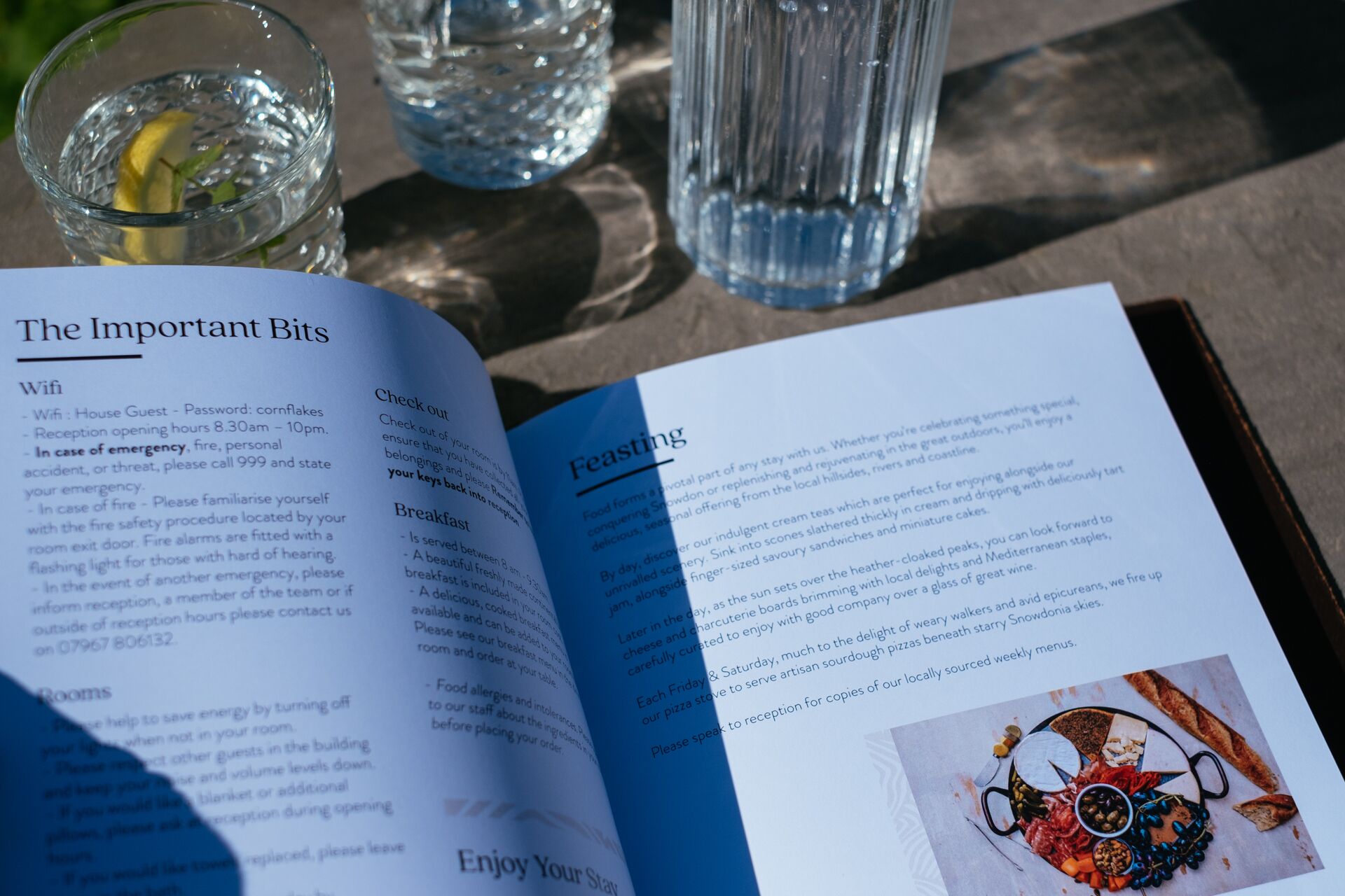 A brochure open on a table with a section titled "The Important Bits" detailing WiFi, check-out, and breakfast information.