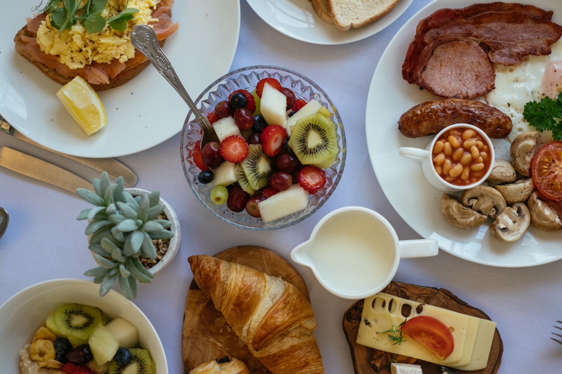A breakfast spread with various dishes including toast, scrambled eggs, bacon, beans, mushrooms, and a fruit bowl.