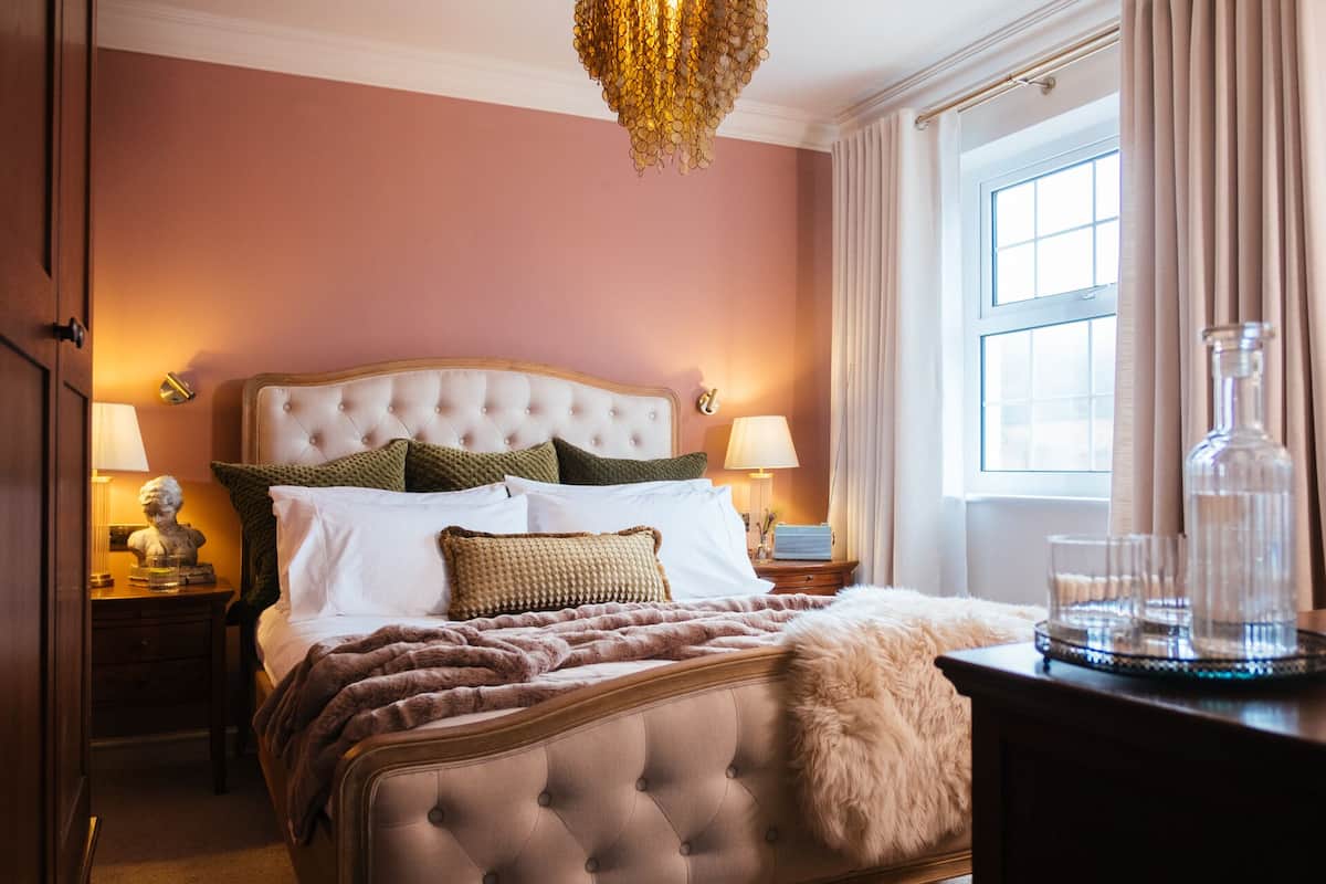 A well-appointed bedroom with a tufted headboard, plush bedding, and a large window with curtains.