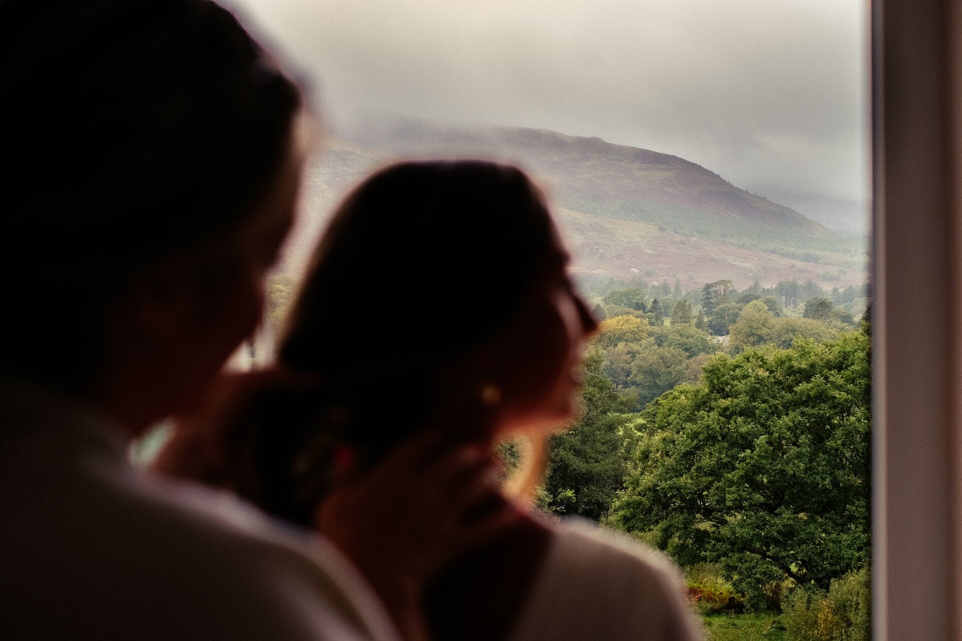 A couple looking out a window at a mountainous landscape with trees.