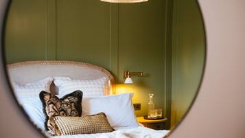 A circular mirror reflecting a neatly made bed with multiple pillows and a bedside table with a lamp and glasses.