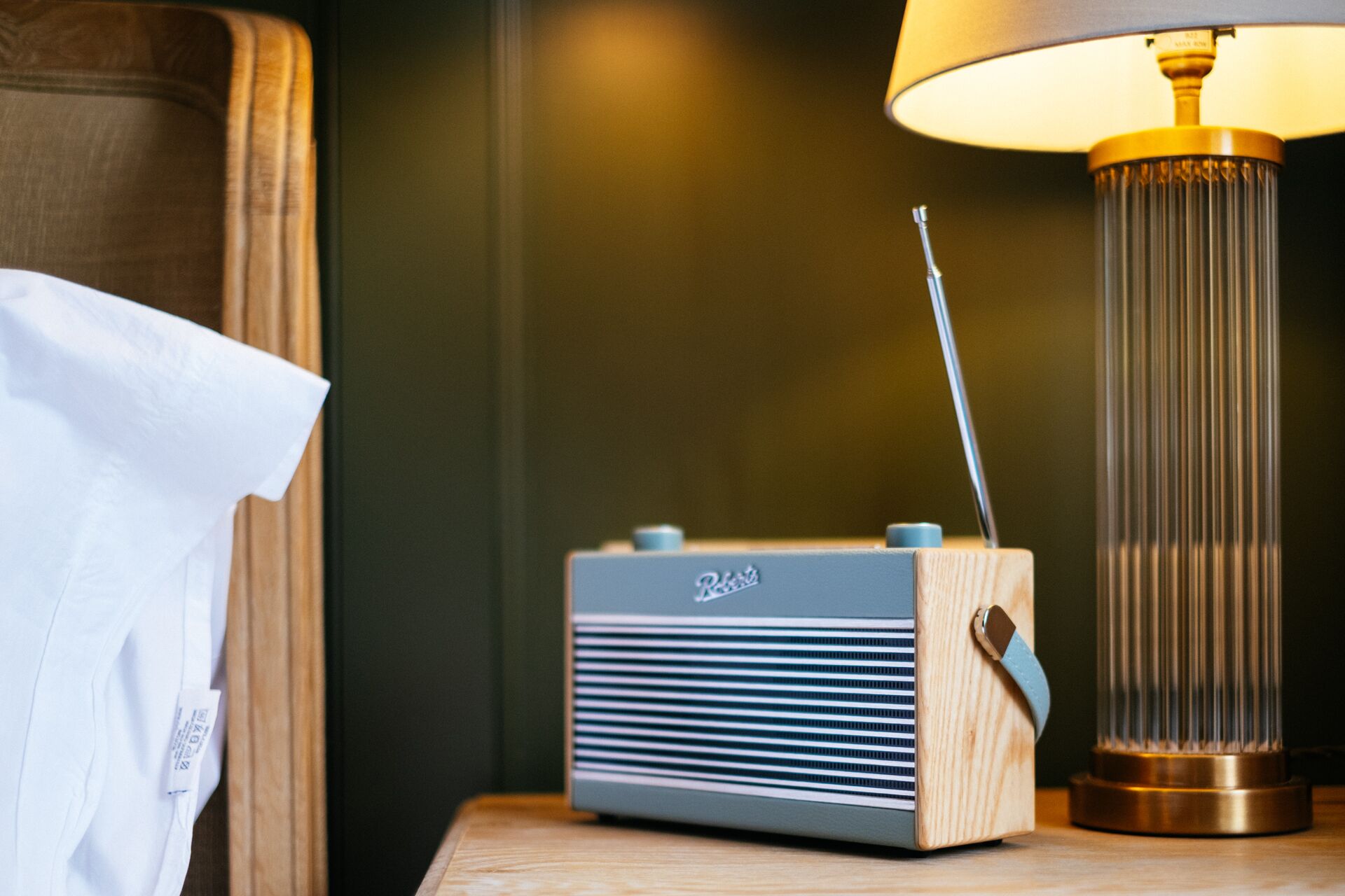A wooden bedside table with a radio and a lamp.