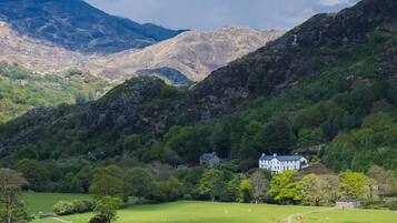 A large white building with a prominent tower, surrounded by lush green fields and mountains in the background.