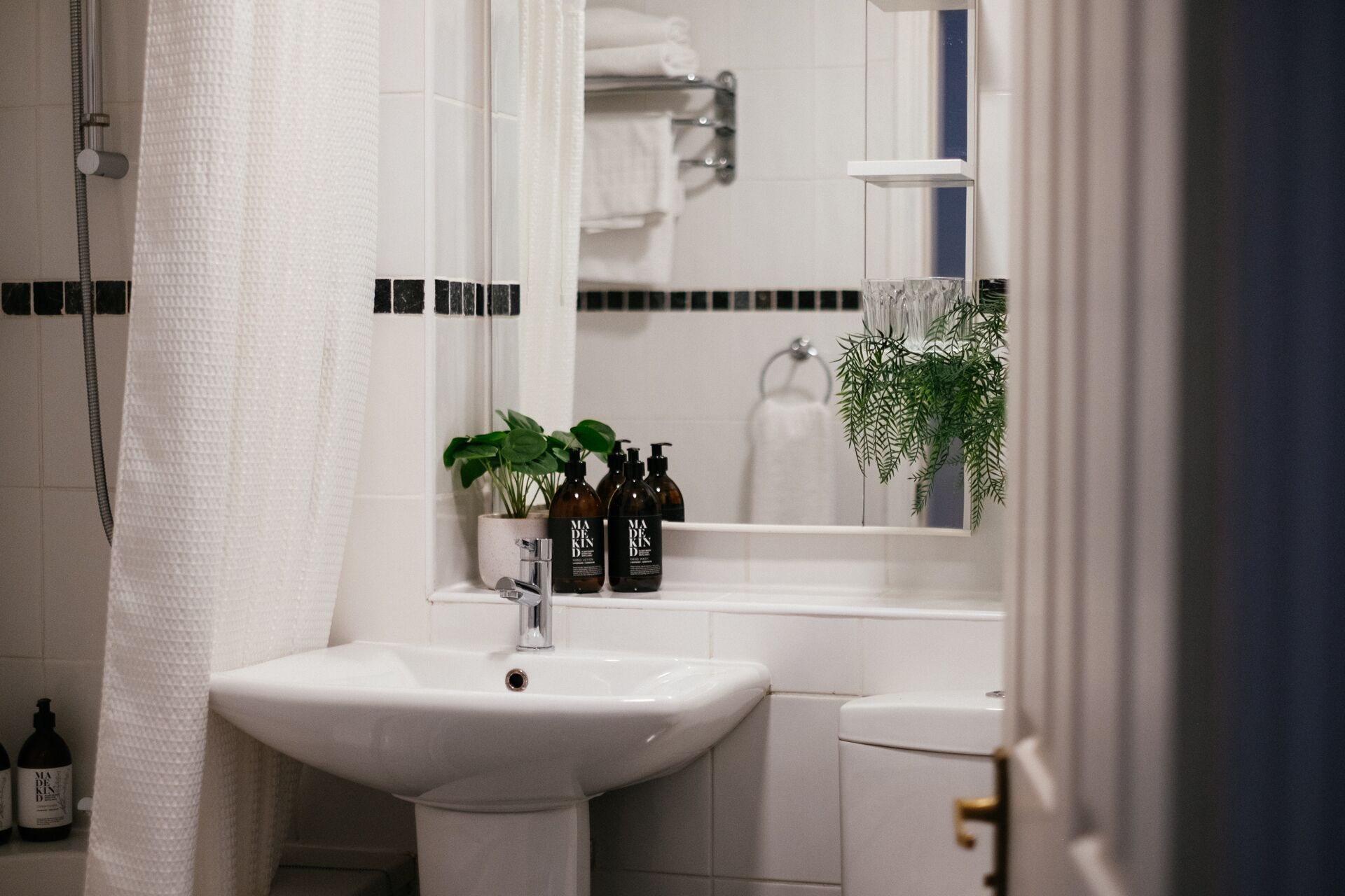 A bathroom with a white sink, a mirror, and a shower curtain. There are bottles of shampoo and conditioner on the sink.