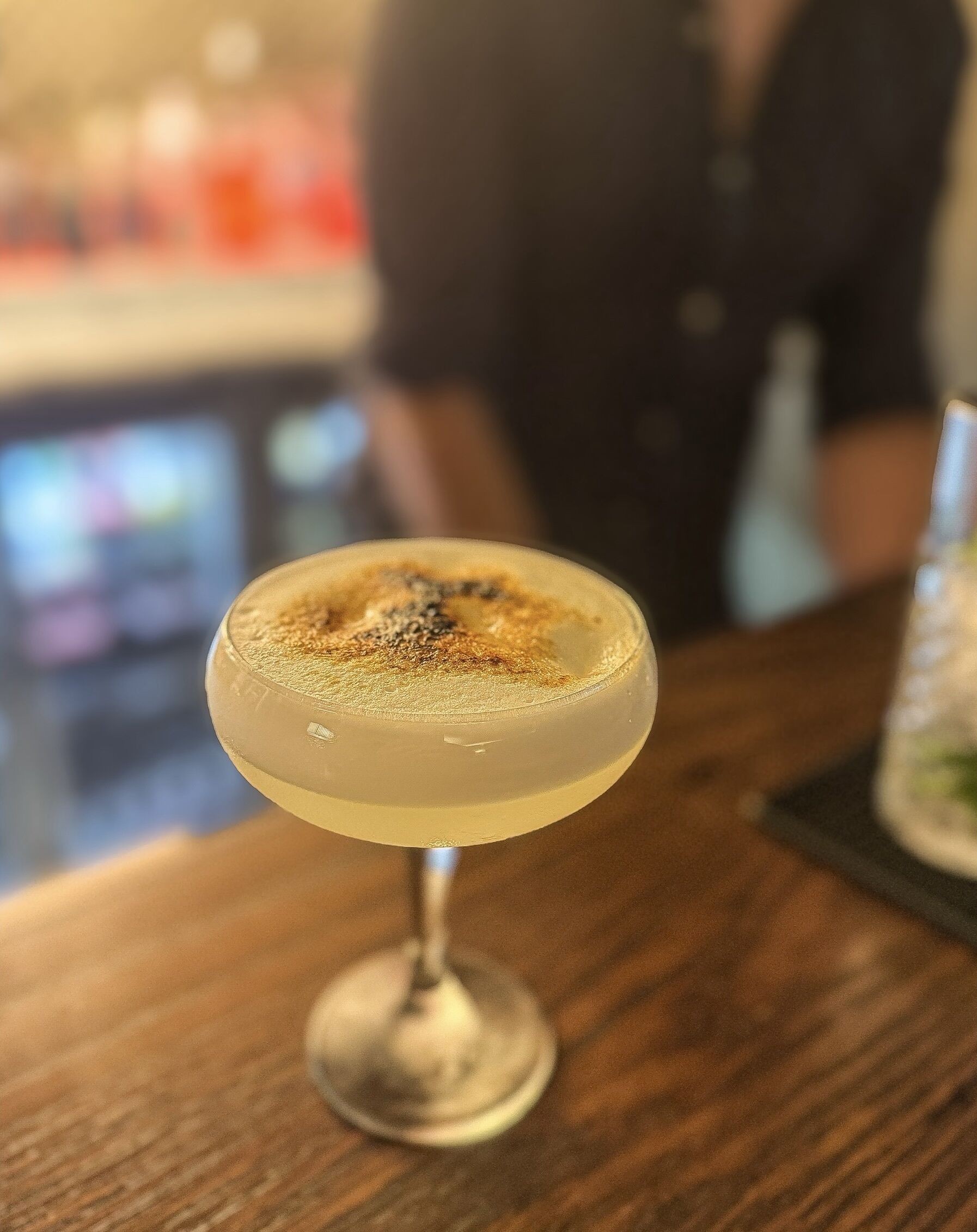 A cocktail in a stemmed glass on a wooden bar counter.