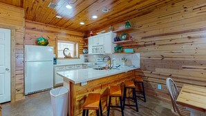 Eine Küche mit Holzwänden, weißen Schränken, einer zentralen Kochinsel mit Hockern und einem Kühlschrank.