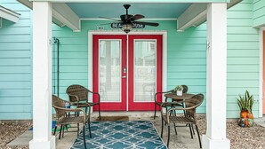 Eine Veranda mit zwei Korbstühlen, einem blauen Teppich mit Muster und einem Deckenventilator.