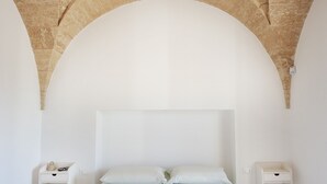 Ein schlicht eingerichtetes Schlafzimmer mit einem großen Bett, zwei Nachttischen und einer gewölbten Steindecke.