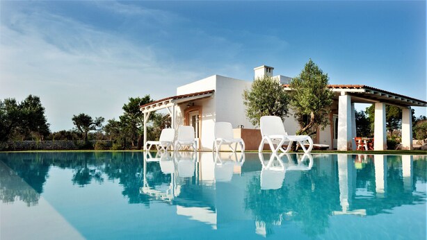 Ein modernes Haus mit Swimmingpool, weißen Liegestühlen und einer Pergola.