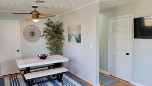 A dining area with a wooden table and bench, a ceiling fan, a wall-mounted decorative item, a potted plant, and a door with a window. - Renovated 2 Bedroom, near VB Vibe district, Surf Park & Dome! (Virginia Beach)