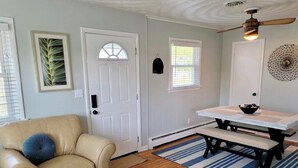 A room with a beige leather chair, a dining table with benches, a white door, and a window with blinds. - Renovated 2 Bedroom, near VB Vibe district, Surf Park & Dome! (Virginia Beach)