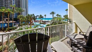 Un balcón con vista a una piscina, palmeras y una playa.