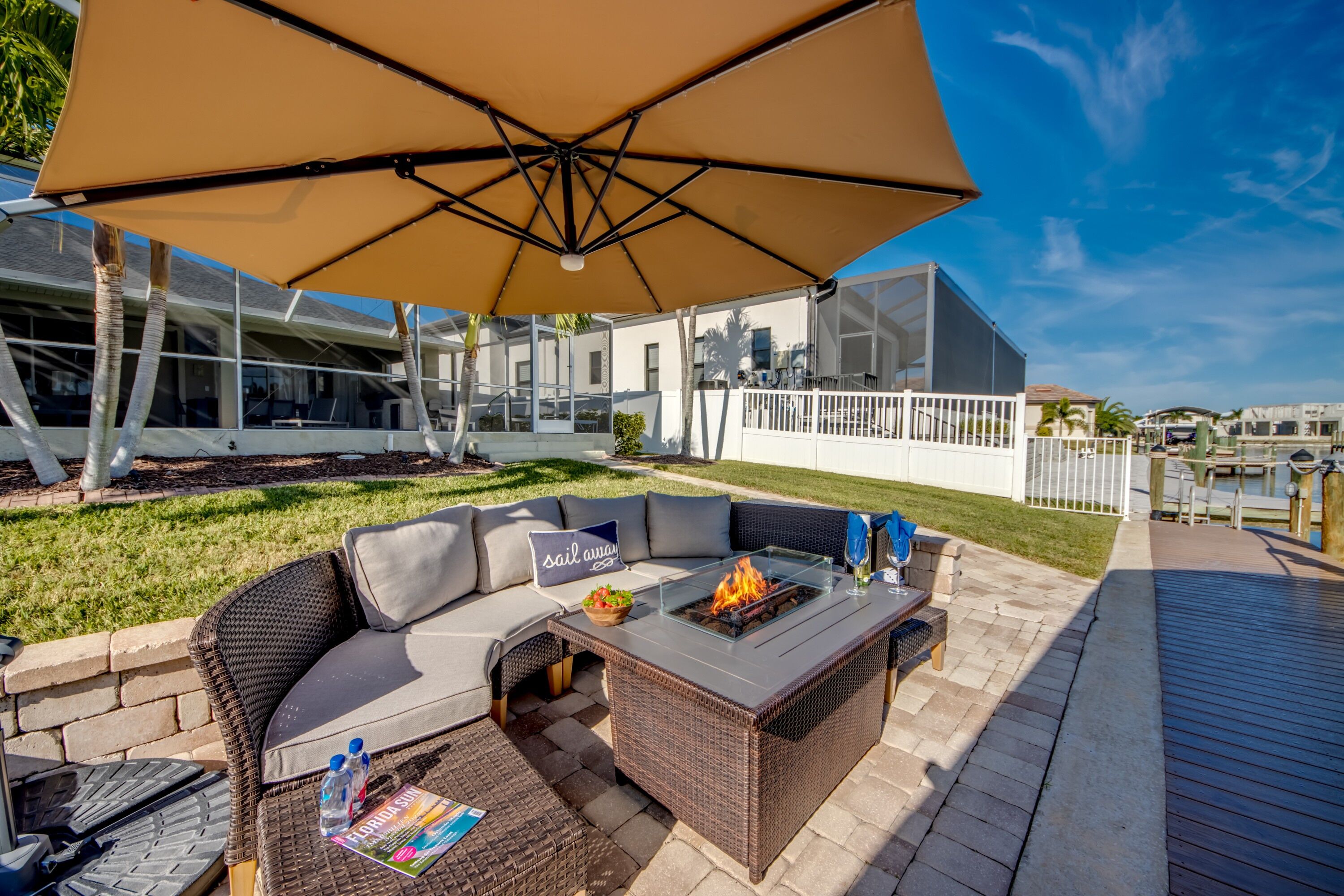 An outdoor patio with a wicker sofa, a glass-top table with a fire feature, and a large umbrella.