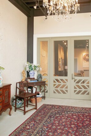 A room with a traditional wooden chair, a table with books and a vase, a patterned rug, and a large door with decorative glass panels. - 4 Luxury Suites in a beautifully restored historic building in Buffalo, Texas.  (Buffalo)