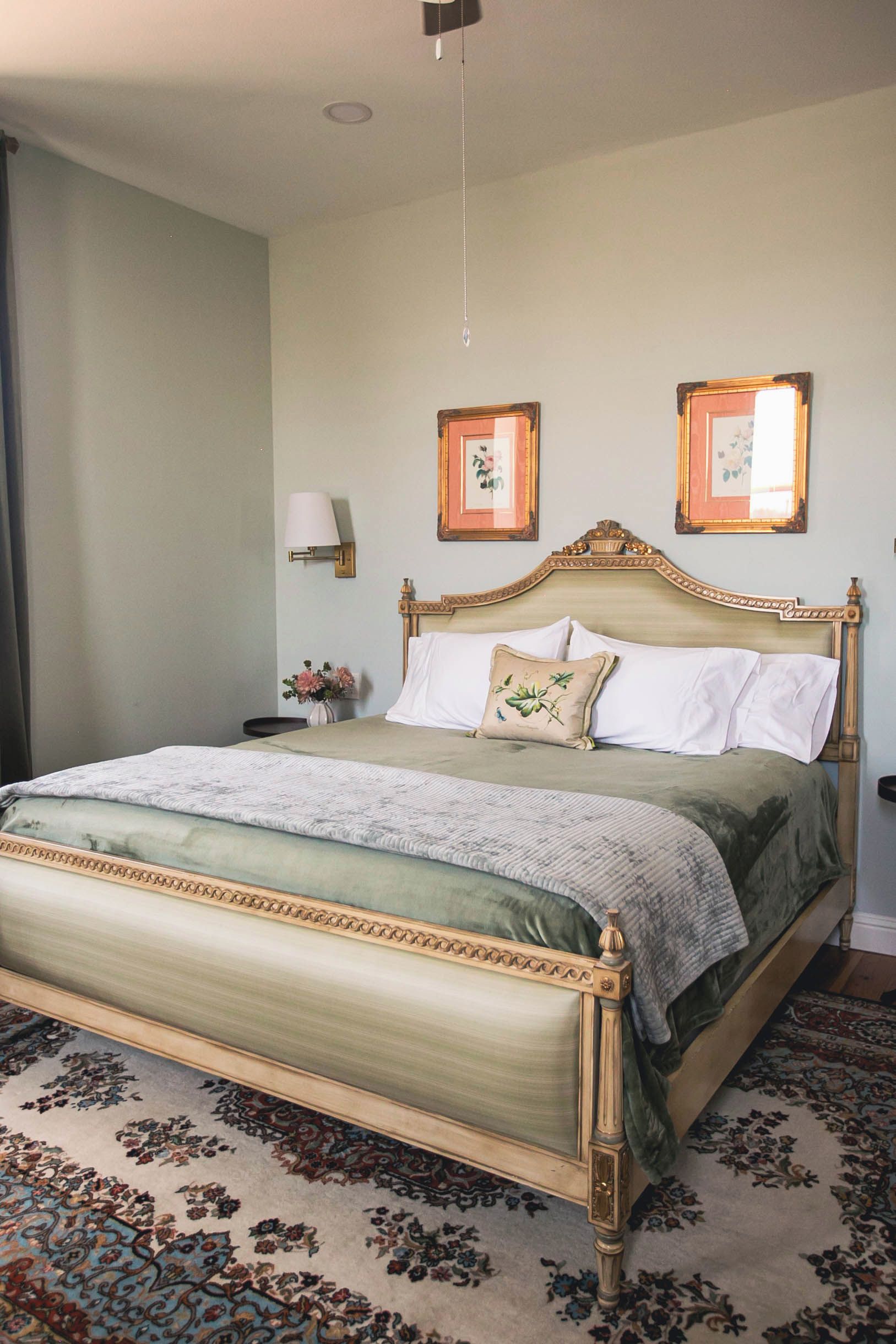 A neatly made bed with a floral-patterned bedspread, a matching headboard, and two wall-mounted lamps.