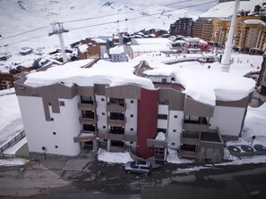 Ein mehrstöckiges Hotel mit Balkonen, ein Sessellift im Hintergrund und verschneite Umgebung.