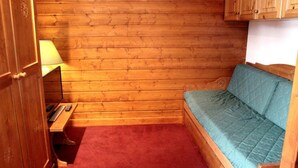 A small, cozy room with wooden walls, a single bed with a blue quilt, a desk with a lamp, and a red carpet. - Ski-in/ski-out & foot of the slopes, 1st floor, view ski slopes, balcony, tv, 32m², Val Thorens (Val Thorens)