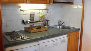 A compact kitchen with wooden cabinets, a microwave, a built-in dishwasher, and a countertop with a grater and other utensils. - Ski-in/ski-out & foot of the slopes, 1st floor, view ski slopes, balcony, tv, 32m², Val Thorens (Val Thorens)